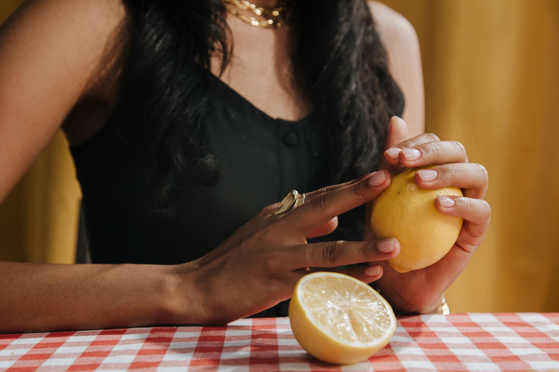 Femme tenant un citron frais à une table à manger, gros plan sur son expression contemplative.