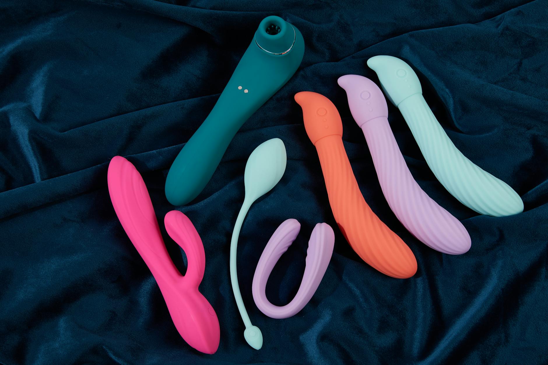 Collection of colorful silicone clitoral vibrators arranged on dark blue fabric