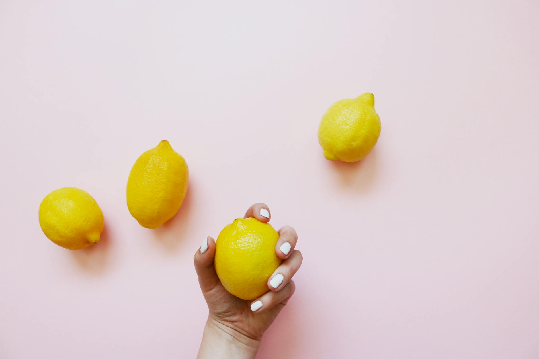 Gros plan d'une main tenant un citron sur un fond rose