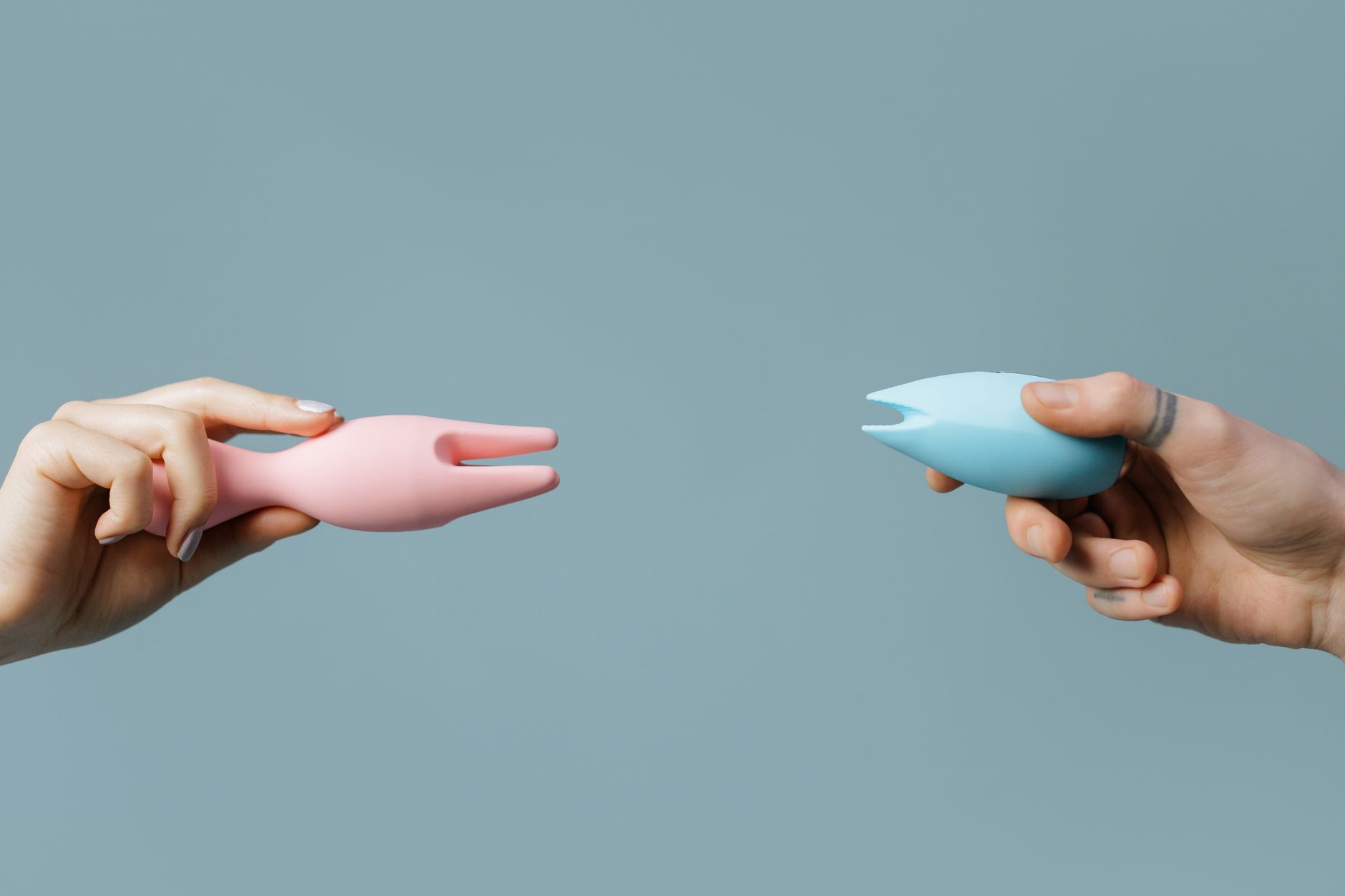 Deux mains tenant des vibromasseurs roses et bleus contre un fond pastel