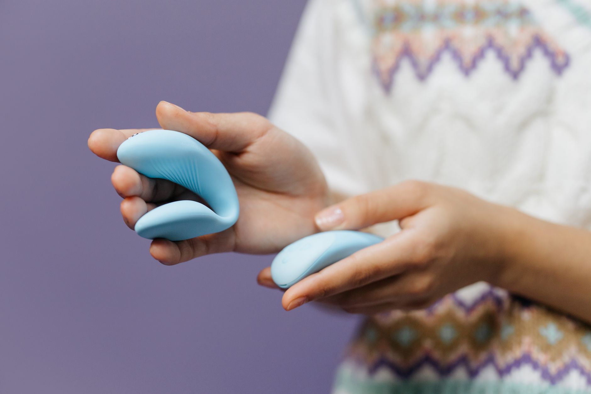 Hand holding a blue lemon clitoral vibrator against a purple background