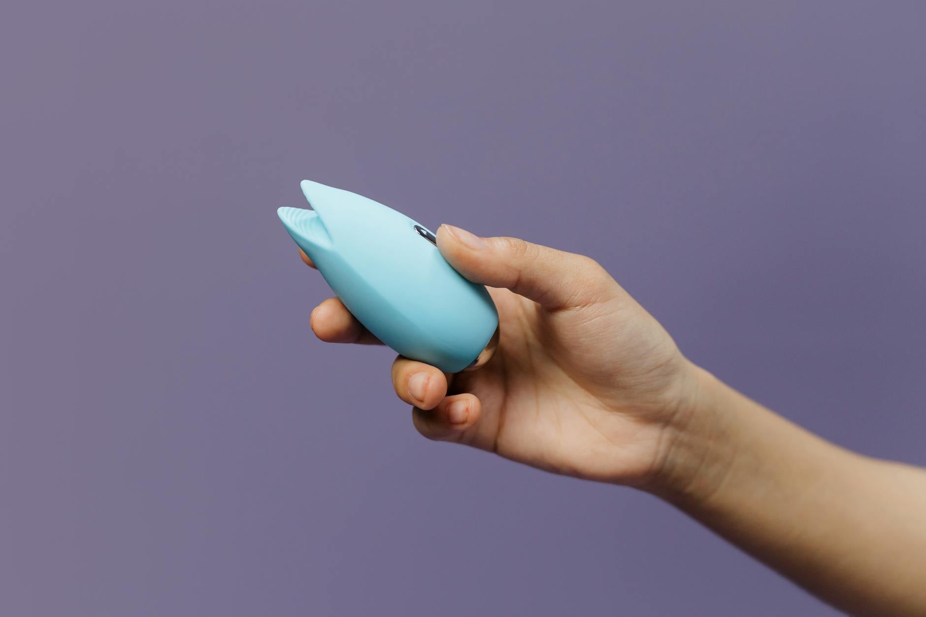 Close-up of a hand holding a vibrator above a decorative glass bowl