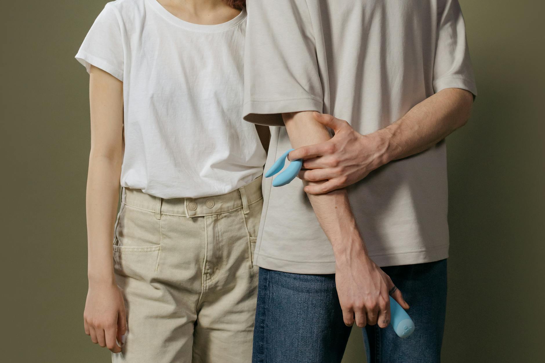 A close-up of hands holding a sleek blue vibrator against a purple background