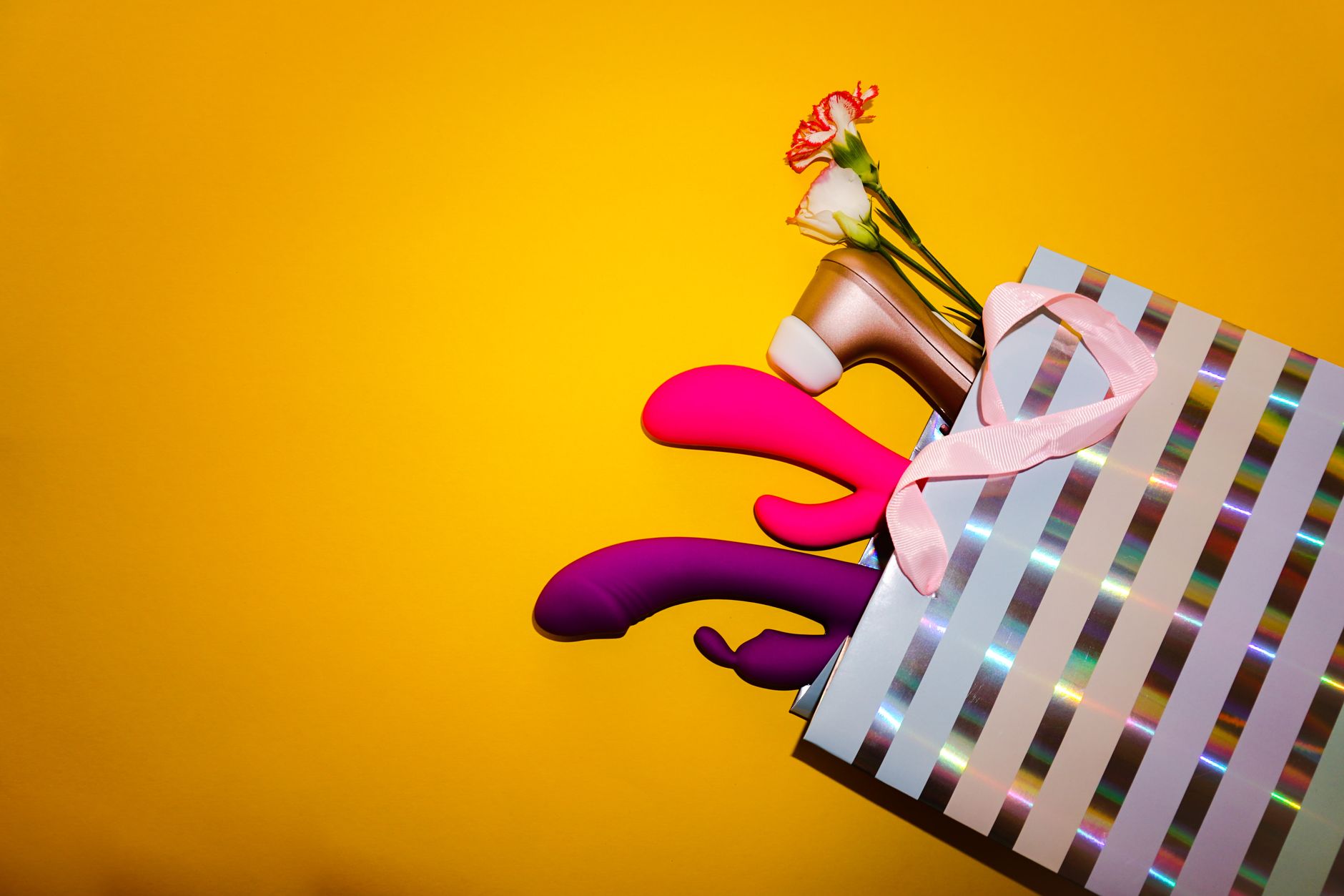 Colorful vibrators with flowers arranged on a bright yellow background, symbolizing a return to sensuality after recovery.